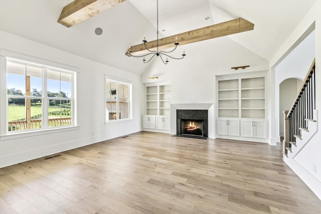 unfurnished living room with built in features, high vaulted ceiling, a chandelier, a high end fireplace, and light wood-type flooring