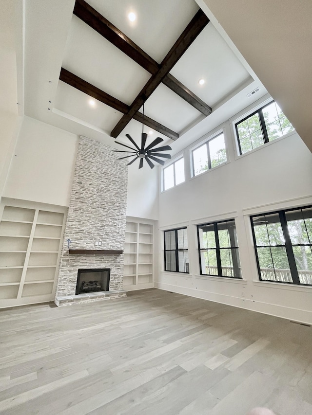 unfurnished living room featuring a stone fireplace, light wood-type flooring, beam ceiling, and a wealth of natural light