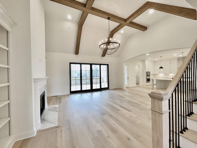 unfurnished living room with light hardwood / wood-style flooring, a premium fireplace, high vaulted ceiling, a notable chandelier, and beamed ceiling