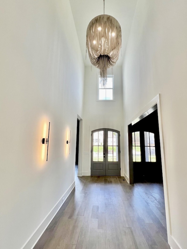 foyer entrance with french doors, wood-type flooring, a high ceiling, and a notable chandelier