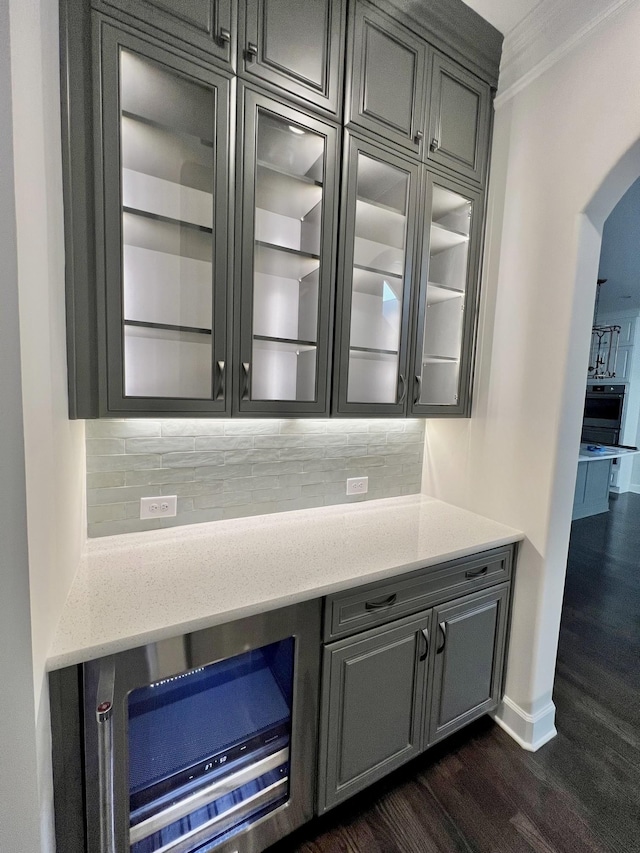 bar featuring dark hardwood / wood-style flooring, backsplash, gray cabinets, and ornamental molding