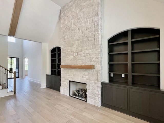 unfurnished living room featuring built in shelves, a fireplace, high vaulted ceiling, and light wood-type flooring