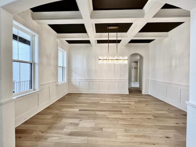 unfurnished dining area with coffered ceiling, beam ceiling, and light hardwood / wood-style floors