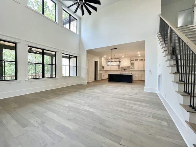 unfurnished living room with ceiling fan with notable chandelier, light hardwood / wood-style floors, and a towering ceiling