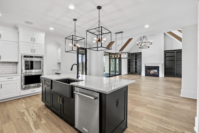 kitchen featuring white cabinetry, appliances with stainless steel finishes, decorative light fixtures, and a center island with sink