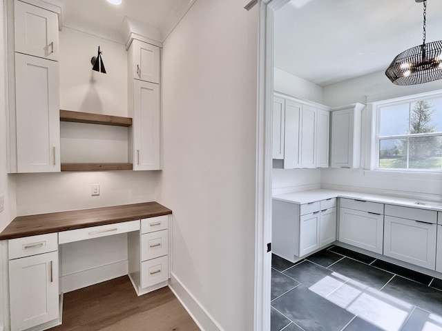 kitchen with wood counters, decorative light fixtures, built in desk, dark hardwood / wood-style floors, and white cabinets