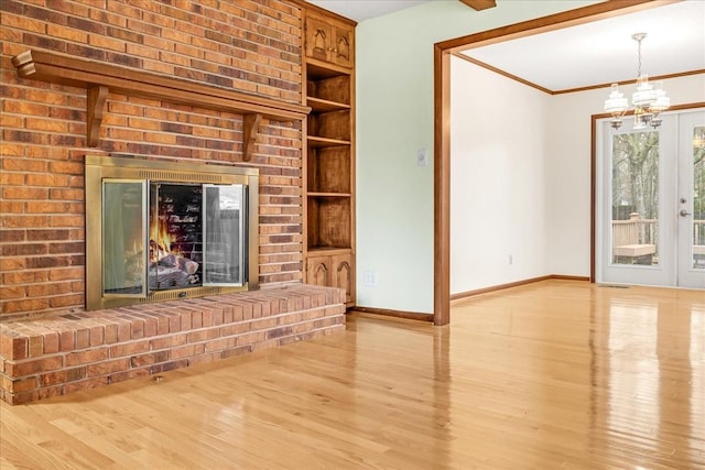 unfurnished living room with a notable chandelier, ornamental molding, a brick fireplace, and light hardwood / wood-style flooring