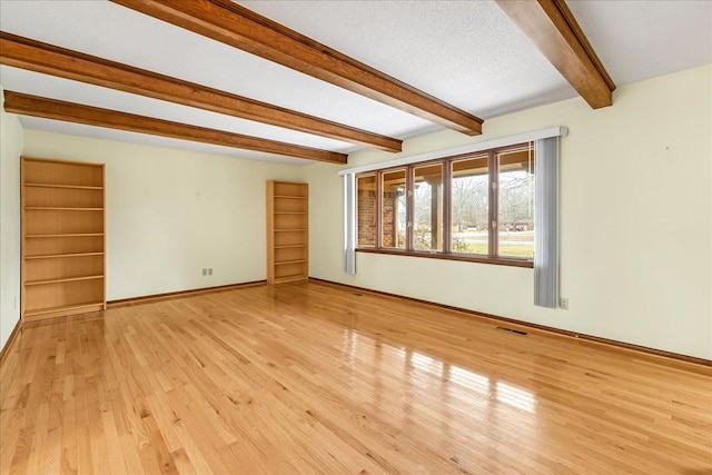 unfurnished room featuring beamed ceiling, a textured ceiling, and light wood-type flooring