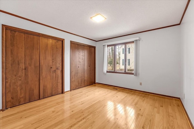 unfurnished bedroom featuring multiple closets, ornamental molding, a textured ceiling, and light wood-type flooring