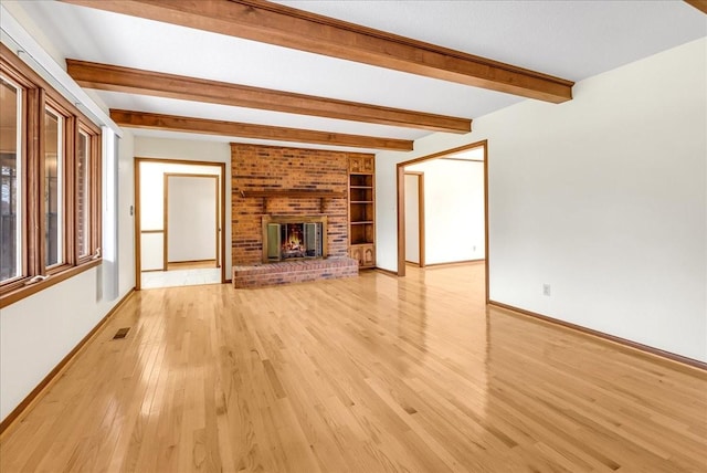 unfurnished living room featuring a brick fireplace, beamed ceiling, and light wood-type flooring