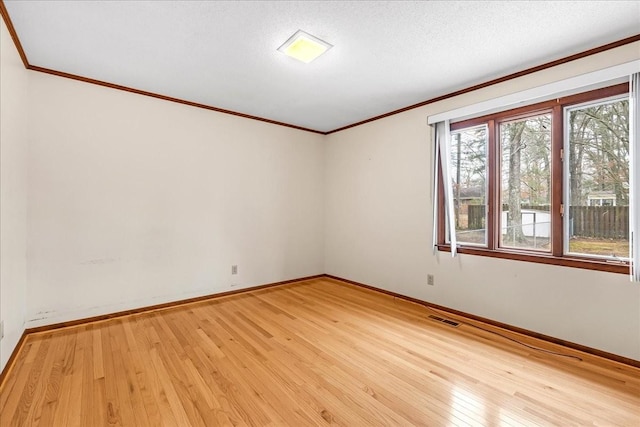 spare room with ornamental molding, a textured ceiling, and light wood-type flooring