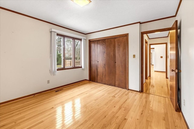 unfurnished bedroom with a closet, ornamental molding, light hardwood / wood-style flooring, and a textured ceiling