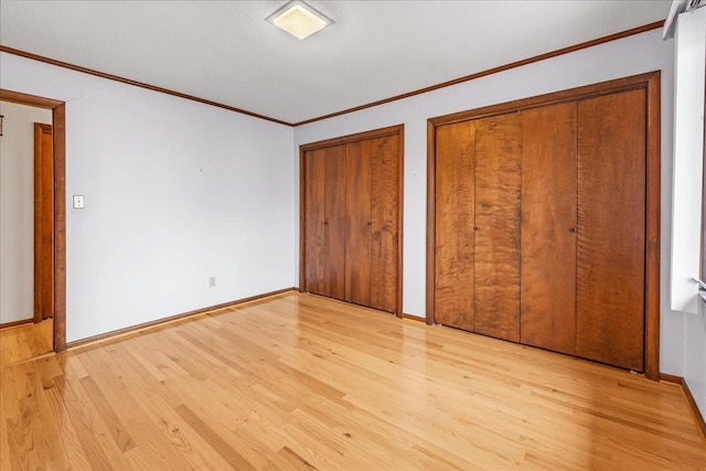 unfurnished bedroom with crown molding, light wood-type flooring, and two closets