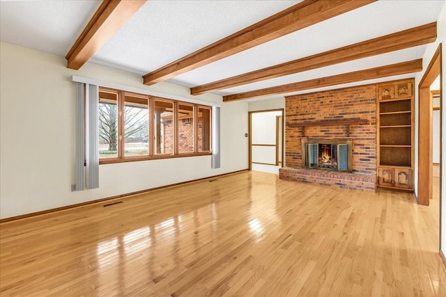 unfurnished living room featuring beamed ceiling, a brick fireplace, a textured ceiling, and light wood-type flooring