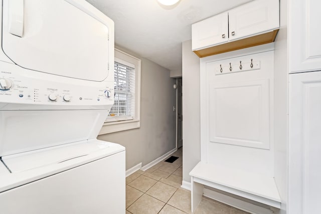 washroom featuring stacked washer and dryer, light tile patterned floors, and cabinets