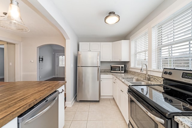 kitchen featuring light tile patterned flooring, white cabinets, wooden counters, hanging light fixtures, and stainless steel appliances