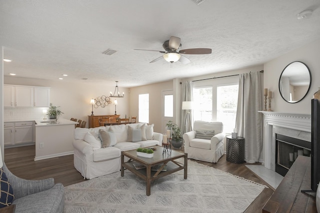 living room featuring ceiling fan with notable chandelier, light hardwood / wood-style floors, a premium fireplace, and a textured ceiling