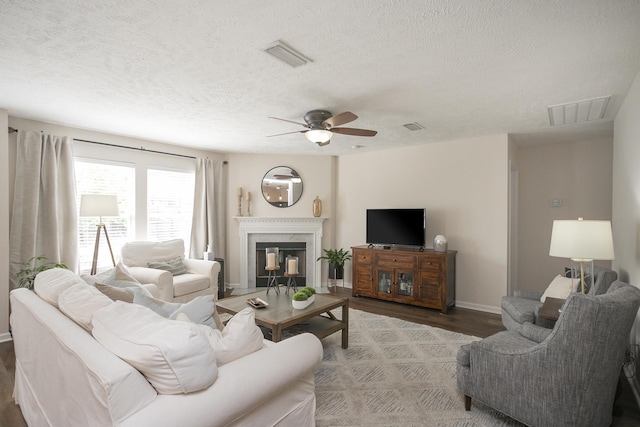 living room with wood-type flooring, ceiling fan, a textured ceiling, and a fireplace