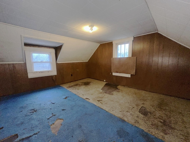 additional living space featuring vaulted ceiling, wood walls, and carpet flooring