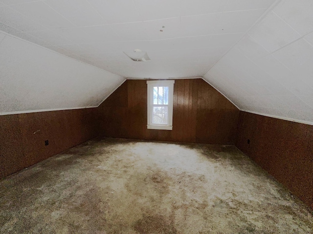 additional living space featuring vaulted ceiling, wood walls, and carpet flooring