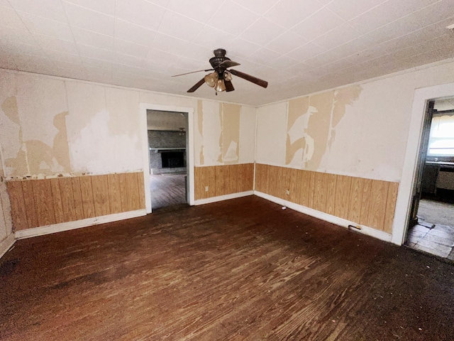 unfurnished room featuring a wainscoted wall, dark wood-style floors, a ceiling fan, and wood walls