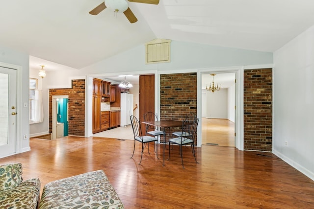 living room featuring brick wall, lofted ceiling, ceiling fan with notable chandelier, and light wood-type flooring