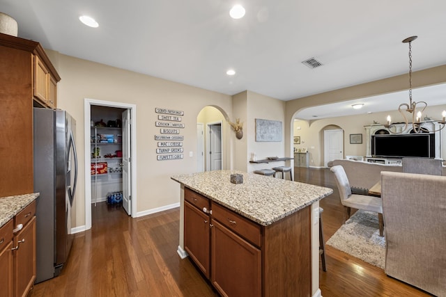 kitchen with light stone counters, stainless steel fridge, a kitchen island, and pendant lighting