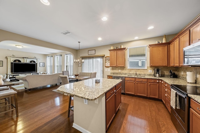 kitchen with appliances with stainless steel finishes, a breakfast bar area, decorative backsplash, hanging light fixtures, and a center island