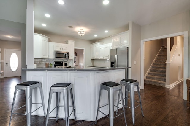 kitchen with dark hardwood / wood-style floors, white cabinets, a kitchen breakfast bar, kitchen peninsula, and stainless steel appliances