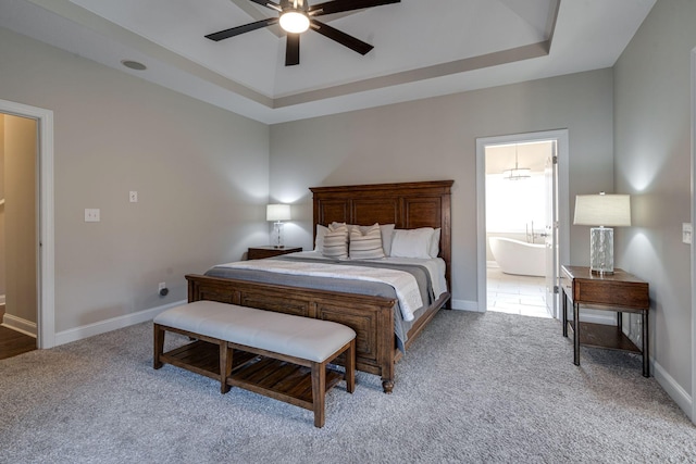 bedroom with ceiling fan, ensuite bath, a tray ceiling, and light carpet