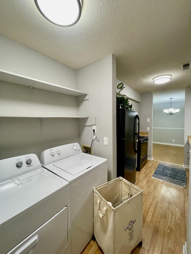 clothes washing area with an inviting chandelier, light hardwood / wood-style floors, washer and dryer, and a textured ceiling