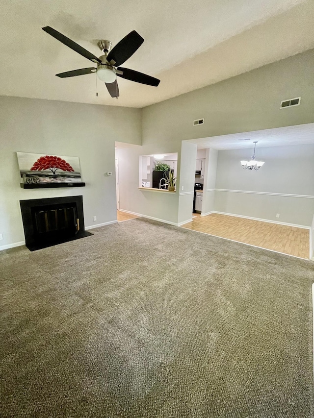 unfurnished living room featuring ceiling fan with notable chandelier, vaulted ceiling, and carpet floors