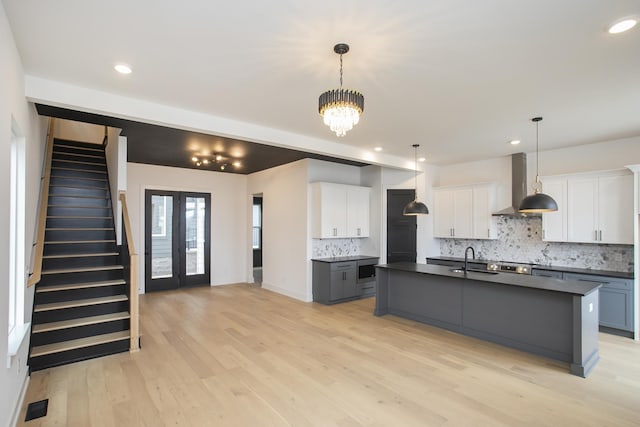 kitchen with hanging light fixtures, white cabinetry, an island with sink, and wall chimney exhaust hood