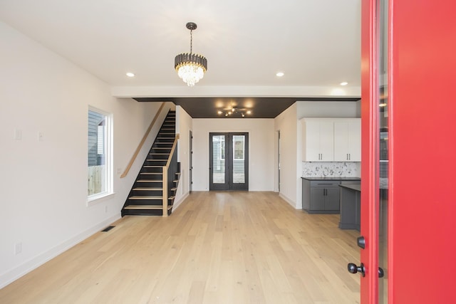 interior space with beamed ceiling, a chandelier, light wood-type flooring, and french doors