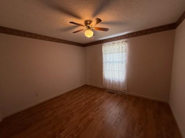 empty room with ceiling fan, dark hardwood / wood-style floors, and a textured ceiling