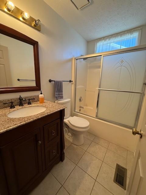 full bathroom featuring combined bath / shower with glass door, tile patterned flooring, vanity, toilet, and a textured ceiling