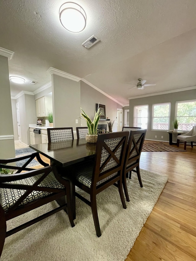 dining space with ceiling fan, ornamental molding, a textured ceiling, and light wood-type flooring