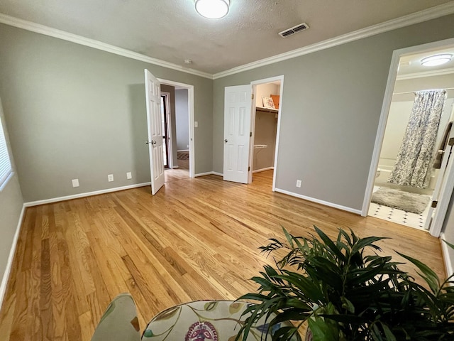 unfurnished bedroom featuring crown molding, a spacious closet, and light hardwood / wood-style flooring