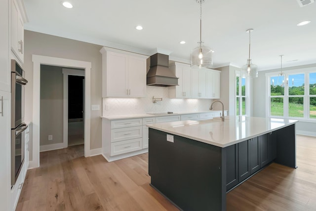 kitchen featuring decorative light fixtures, custom range hood, white cabinets, and a large island