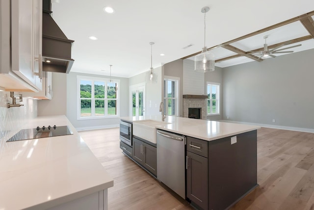 kitchen featuring appliances with stainless steel finishes, a kitchen island with sink, a fireplace, and decorative light fixtures