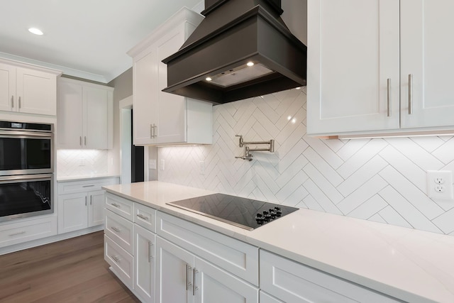 kitchen with white cabinetry, custom range hood, black electric cooktop, decorative backsplash, and stainless steel double oven