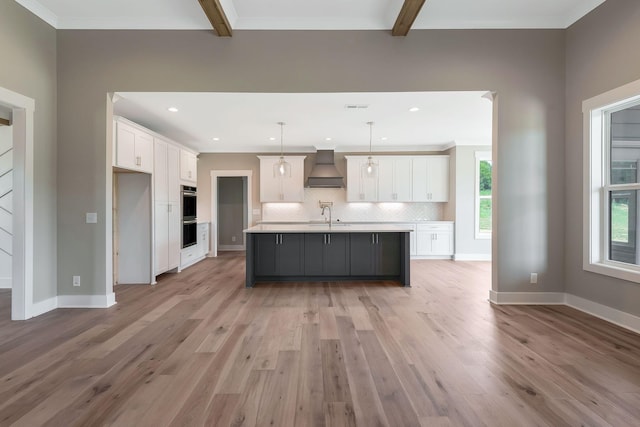 kitchen featuring premium range hood, white cabinetry, a kitchen island with sink, and hanging light fixtures