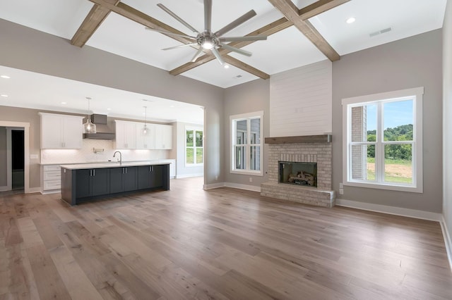 unfurnished living room featuring a fireplace, wood-type flooring, beamed ceiling, and ceiling fan