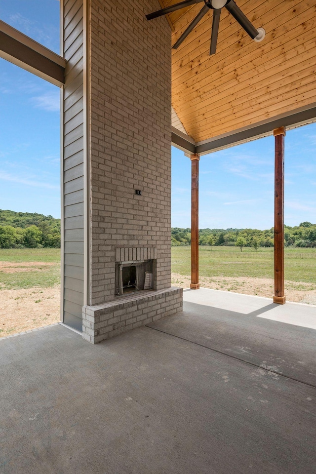 view of patio featuring an outdoor brick fireplace, a rural view, and ceiling fan