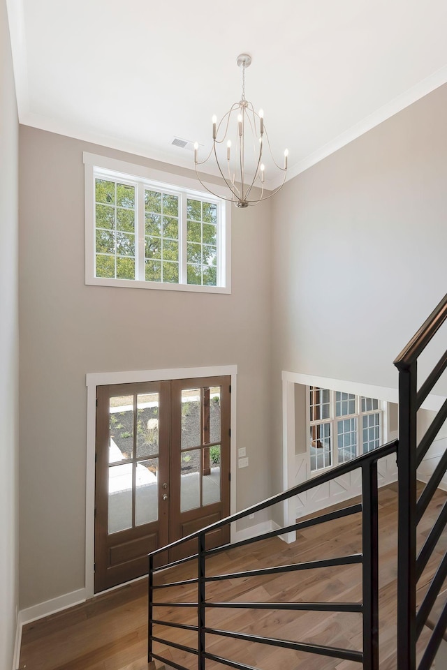 stairs with a notable chandelier, crown molding, wood-type flooring, and french doors