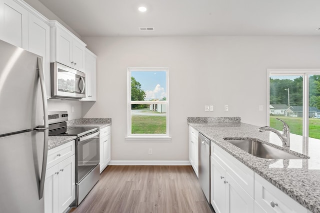 kitchen with plenty of natural light, white cabinetry, sink, stainless steel appliances, and light stone countertops