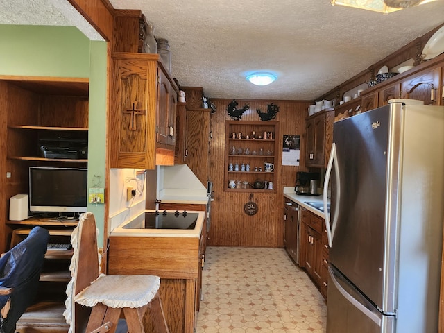 kitchen featuring stainless steel refrigerator, black electric stovetop, wooden walls, and a textured ceiling