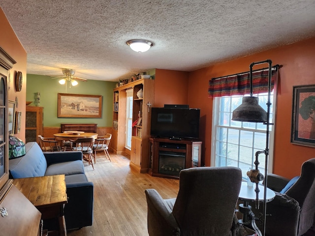 living room with ceiling fan, a textured ceiling, and light wood-type flooring