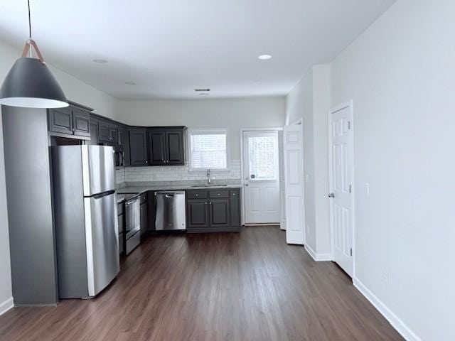 kitchen with appliances with stainless steel finishes, pendant lighting, tasteful backsplash, sink, and dark hardwood / wood-style flooring