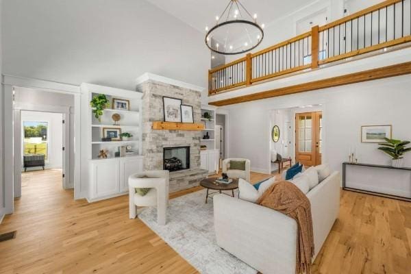 living room featuring an inviting chandelier, a towering ceiling, a stone fireplace, and light hardwood / wood-style flooring